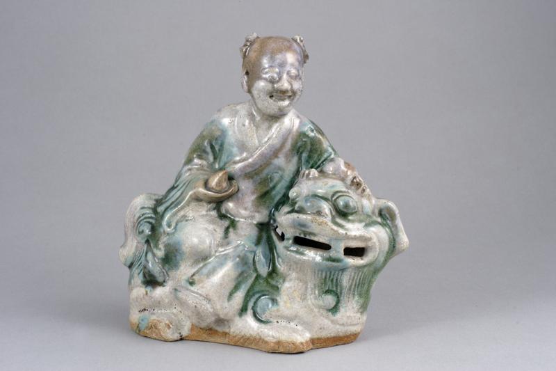 Boy holding a peach, seated on a Lion-dog